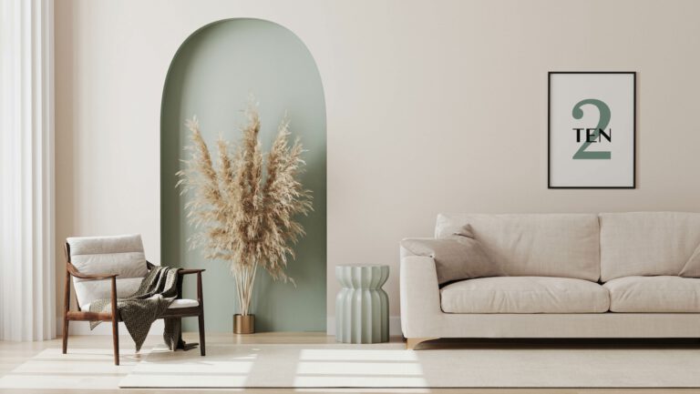 A minimalist living room with a neutral color palette featuring a sofa, armchair, decorative pampas grass, arched alcove, and a framed number ten artwork.